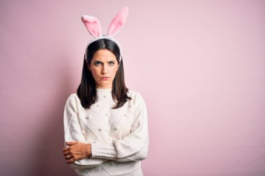 Pembe izole edilmiş arka planda sevimli paskalya tavşanı kulakları takan beyaz bir kadın şüpheci ve gergin, yüzünde çapraz kollu tasvip etmeyen bir ifade. Negatif kişi.