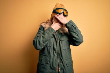 Orta yaşlı güzel sarışın kayakçı kadın kar sporu giysisi ve kayak gözlüğü takıyor gözleri ve ağzı kapalı, şaşırmış ve şok olmuş. Duygularını gizliyor.