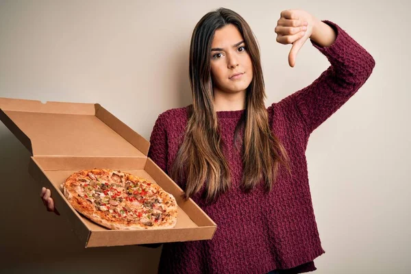 年轻美丽的姑娘拿着意大利披萨盒 站在苍白的背景上 满脸怒容 负面的迹象表明她不喜欢大拇指朝下 拒绝的概念 — 图库照片