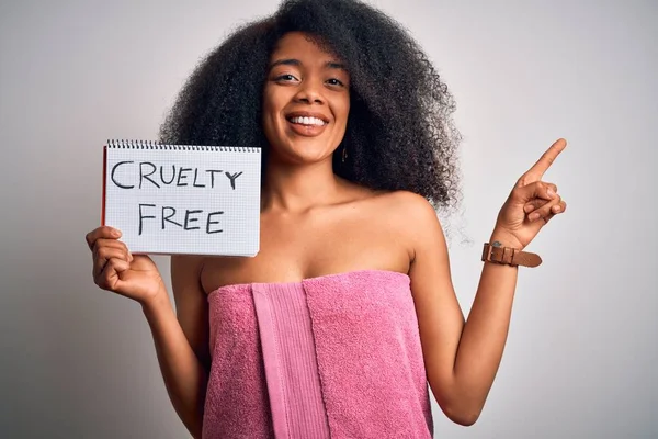 Young african american woman with afro hair wearing a towel asking for cruelty free beauty very happy pointing with hand and finger to the side