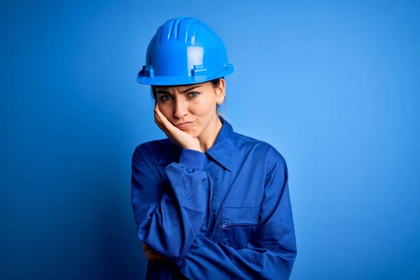 Young beautiful worker woman with blue eyes wearing security helmet and uniform thinking looking tired and bored with depression problems with crossed arms.