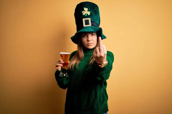 若いです美しいです女性身に着けています緑の帽子飲むガラスのビール上の聖人のパティック日表示中指 不礼儀正しいと無礼なファックオフ式 — ストック写真