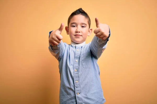 黄色の隔離された背景の上に立つエレガントなシャツを着ている若い男の子は 手で積極的なジェスチャーをすることを承認し 親指を上げて笑顔と成功のために幸せ 勝者のジェスチャー — ストック写真