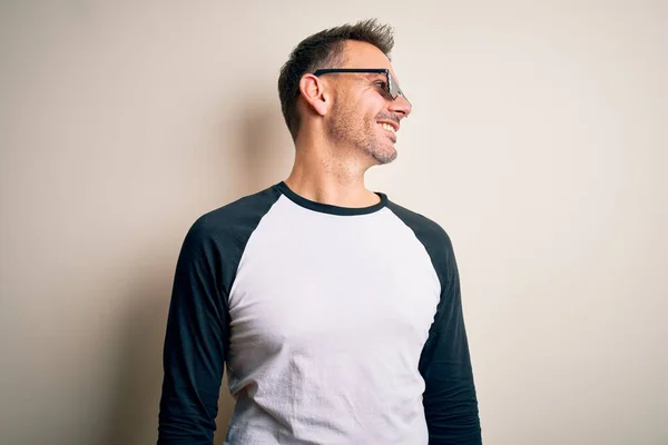 Young handsome man wearing funny thug life sunglasses meme over white background looking away to side with smile on face, natural expression. Laughing confident.