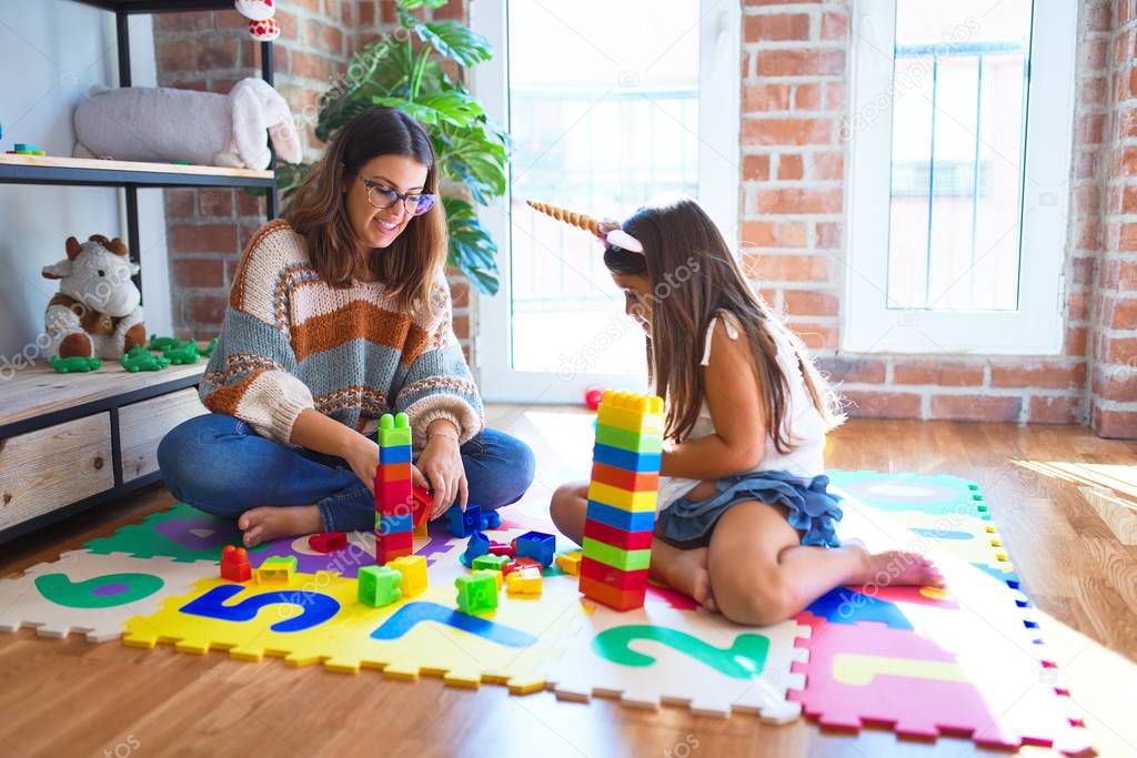 Beautiful teacher and toddler playing with building blocks toy around lots of toys at kindergarten