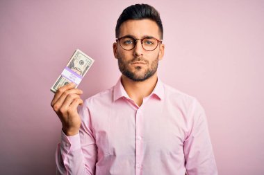 Genç iş adamının elinde 20 dolarlık banknotlar var. Pembe izole bir geçmişi var. Akıllı bir yüz ifadesiyle ciddi ciddi düşünüyor.