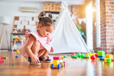 Genç, güzel bir çocuk yerde oturmuş anaokulunda tahta tren oyuncağıyla oynuyor.