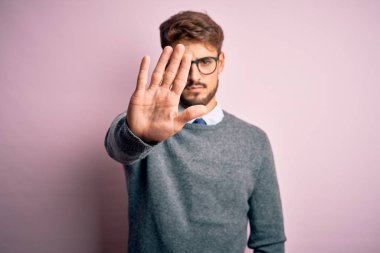 Gözlüklü, pembe arka planda duran, sakallı ve kazaklı genç yakışıklı adam avucunun içi gibi şarkı söylemeyi kesiyor. Yüzünde olumsuz ve ciddi bir jest olan uyarı ifadesi.