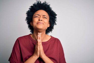 Young beautiful African American afro woman with curly hair wearing casual t-shirt standing begging and praying with hands together with hope expression on face very emotional and worried. Begging. clipart