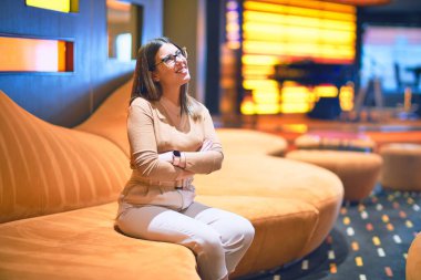 Mutlu ve kendinden emin gülümseyen genç ve güzel bir kadın. Barda yüzünde gülümsemeyle kanepede oturmak.