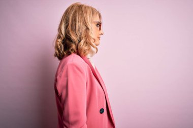 Orta yaşlı güzel sarışın iş kadını zarif pembe ceket ve gözlük takan rahat profil pozu veren kendine güvenen bir gülümsemesi olan..