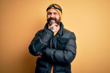 Sakallı, kar maskesi takmış, kar maskesi takmış ve kayak gözlüklü yakışıklı kayakçı kolları çaprazlanmış ve elleri çenesinde kaldırılmış bir şekilde kameraya gülümsüyor. Olumlu düşünüyorum..