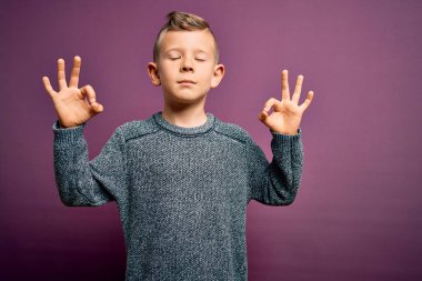 Mor arka plan üzerinde duran mavi gözlü küçük beyaz çocuk rahatla ve gözleri kapalı meditasyon yaparken parmaklarınla gülümse. Yoga konsepti.