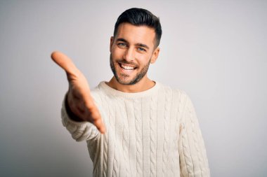 İzole edilmiş beyaz arka planda sıradan bir süveter giyen yakışıklı genç bir adam dostça bir selamlama ve hoş geldin hediyesi olarak el sıkışma sunuyor. Başarılı bir iş..