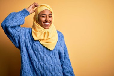 Genç Afrikalı Afro kadın, izole edilmiş sarı arka plan üzerine Müslüman başörtüsü takıyor ve soru sormayı merak ediyor. Şüpheyle kararsız, kafa kafaya düşünerek. Düşünceli kavram.