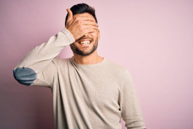 Soyutlanmış pembe arka planda dikilen sıradan bir süveter giyen genç yakışıklı. Gülümseyen ve gülümseyen bir adam. Kör kavram.