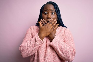 Pembe arka planda günlük süveter giyen Afrikalı Amerikalı artı cüsseli kadın yanlışlıkla ağızlarını kapatarak şok geçirdi. Gizli konsept.