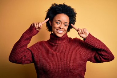 Kıvırcık saçlı, balıkçı yaka kazaklı, iki eliyle başını gösteren gülümseyen güzel Afro-Amerikan kadın. Harika bir fikir ya da düşünce, iyi bir hafıza.