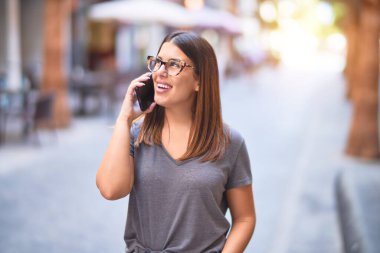 Mutlu ve kendinden emin gülümseyen genç ve güzel bir kadın. Yüzünde gülümsemeyle kasaba caddesinde akıllı telefonun başında konuşmak.