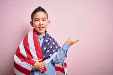 Amerika Birleşik Devletleri bayrağına sarılı küçük vatansever çocuk bağımsızlık gününde elini ve parmağını yana uzatarak mutlu mesut işaret ediyor.