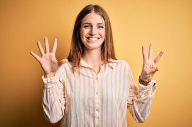 Genç, güzel, kızıl saçlı bir kadın, sarı arka planda günlük çizgili gömlek giyiyor. Sekiz numaralı parmaklarıyla işaret ediyor. Kendinden emin ve mutlu bir şekilde gülümsüyor..