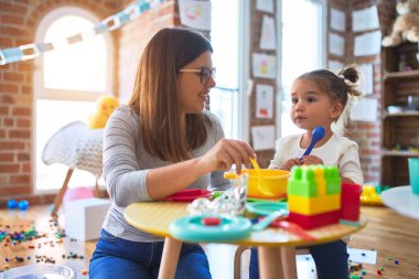 Anaokulunda plastik yemek ve çatal bıçakla oynayan genç ve güzel öğretmen ve bebek.