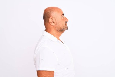 Orta yaşlı yakışıklı bir adam şık bir gömlek giyiyor. İzole edilmiş beyaz arka plan üzerinde duruyor. Yan tarafa bakıyor, rahat bir görünüm sergiliyor..