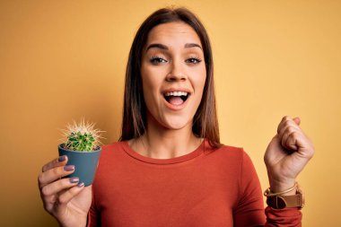 Sarı arka planda küçük kaktüsler tutan genç, güzel esmer kadın gururla bağırıyor ve zaferi ve başarıyı kutluyor. Çok heyecanlı, coşkulu bir duygu.