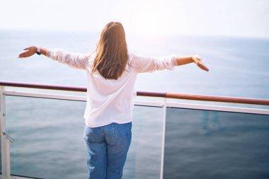 Genç ve güzel bir kadın gemide ayakta duruyor. Yüzünde gülümseme ve kollarını geriye doğru açıp gemi gezisi yapıyor.
