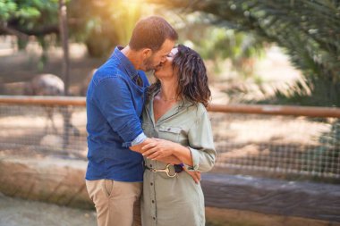 Şehir parkında mutlu ve kendinden emin gülümseyen orta yaşlı güzel bir çift. Yüzünde gülümsemeyle ayakta durup sarılıp öpüşmek.