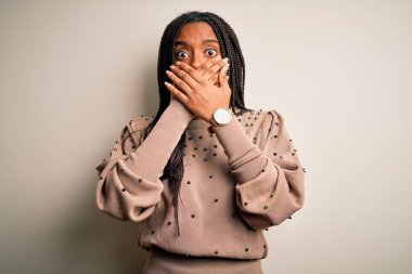 Genç Afro-Amerikalı moda kadını kahverengi izole arka planda gündelik ayakta dikilirken ağzı yanlışlıkla ellerle kapatırken şok oldu. Gizli konsept.