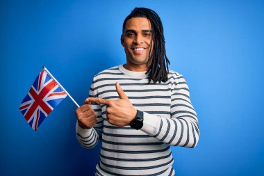 Genç Afro-Amerikan vatansever adam elinde Birleşik Krallık bayrağı tutarken mutlu bir şekilde el ve parmağı işaret ediyor.