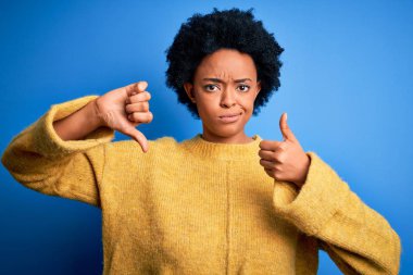 Kıvırcık saçlı, sarı kazaklı, güzel Afro-Amerikan bir kadın. Baş parmak hareketi yapıyor, anlaşmazlık ve anlaşma ifadesi takınıyor. Çılgın çatışma