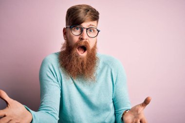 Pembe izole edilmiş arka planda gözlük takan yakışıklı, kızıl saçlı, neşeli, güler yüzlü, dost canlısı, olumlu ve kendinden emin bir selamlama.
