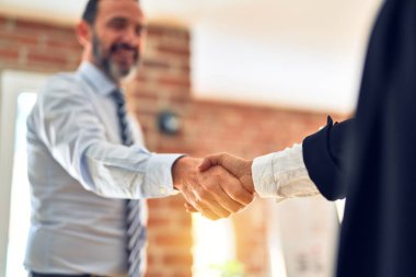 Mutlu ve kendinden emin gülümseyen iki orta yaşlı iş adamı. Birlikte çalışırken gülümseyerek ofiste el sıkışırken.