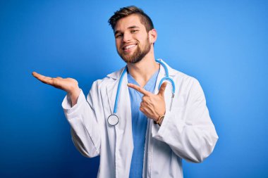 Sakallı, mavi gözlü, beyaz önlüklü, steteskop takmış genç sarışın doktor kameraya hayret ediyor ve gülümsüyor..