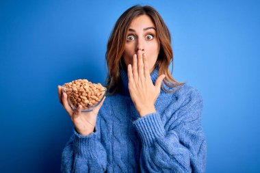 Genç ve güzel esmer bir kadın elinde fındık kabıyla mavi arka planda kaplama ağzı hata yüzünden utançla dolu, korkunun ifadesi, sessizlikten korkan, gizli bir konsept