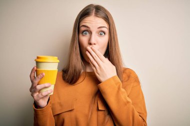 Genç, güzel, kızıl saçlı bir kadın izole edilmiş beyaz arka planda bir fincan kahve içiyor. Ağzı kapalı, utancından ağzı açık, korkusunun dışa vurumu, sessizlikten korkması, gizli bir konsept.