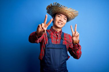 Önlük takmış, mavi arka planda hasır şapka takmış genç, yakışıklı bir çiftçi kameraya bakıp zafer işareti yapıyor. İki numara..