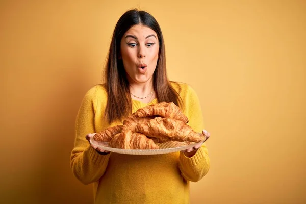 Młoda Piękna Kobieta Trzymająca Francuskie Ciasto Croissant Żółtym Tle Przerażona — Zdjęcie stockowe