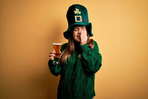 若いです美しい女性を身に着けています緑の帽子を飲みますビールのガラスの上に聖人の公園の日笑いと恥ずかしいクスクス笑いの手で口をカバー ゴシップやスキャンダルの概念 — ストック写真