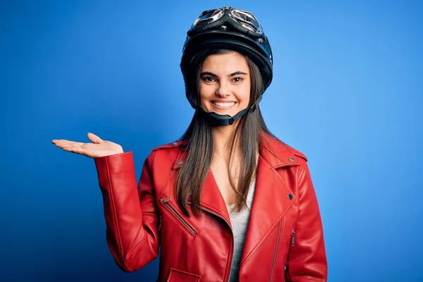 若いです美しいですブルネットオートバイのヘルメットとジャケットを身に着けている女性は陽気なプレゼンテーションを笑顔し カメラを見て手の手のひらで指して — ストック写真