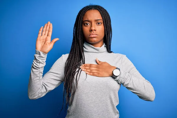 Young african american woman standing wearing casual turtleneck over blue isolated background Swearing with hand on chest and open palm, making a loyalty promise oath