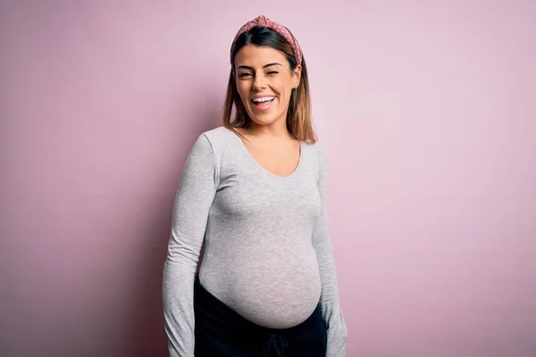 若いです美しいですブルネット女性妊娠期待しています赤ちゃん上の隔離されたピンクの背景ウィンク見ますザカメラとともにセクシー式 陽気で幸せな顔 — ストック写真