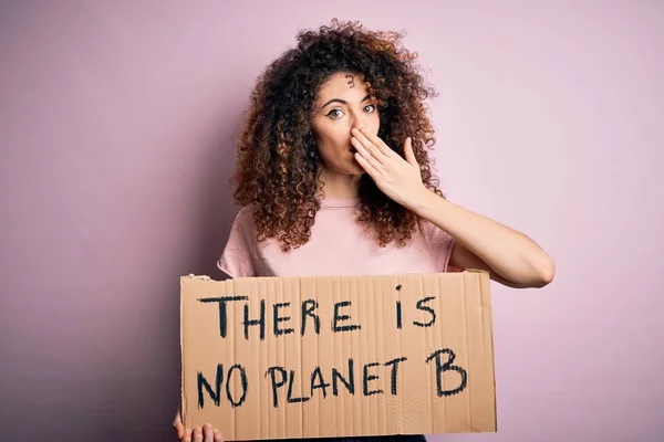 Young beautiful activist woman with curly hair and piercing protesting asking for change planet cover mouth with hand shocked with shame for mistake, expression of fear, scared in silence, secret concept