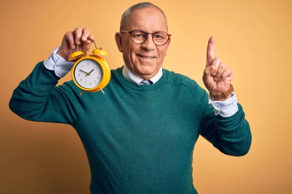 Senior Stilig Man Som Håller Väckarklocka Stående Över Isolerad Gul — Stockfoto