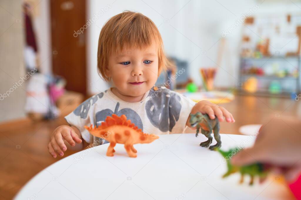 Adorable toddler playing with dinosaurs around lots of toys at kindergarten