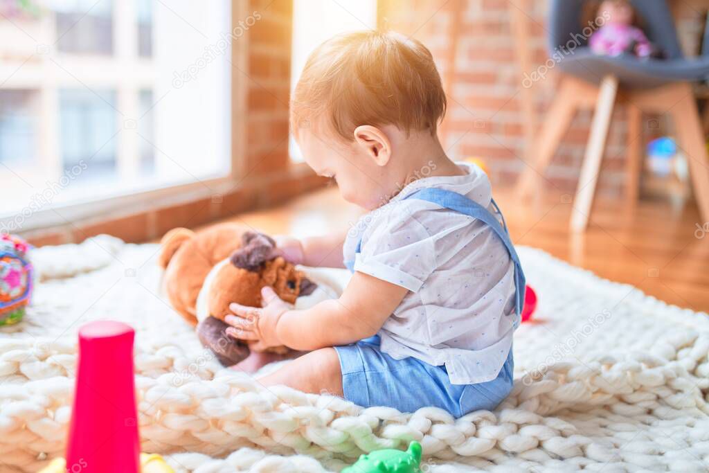 Beautiful toddler sitting on the blanket playing with dog doll at kindergarten