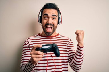 Sakallı yakışıklı oyuncu joystick ve kulaklık kullanarak video oyunu oynuyor. Gururla bağırıyor, zaferi kutluyor ve başarıyı kutluyor. Çok heyecanlı, coşkulu bir duygu.