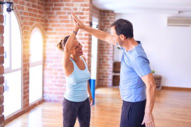 Orta yaşlı güzel sporcu çift mutlu gülümsüyor. Yüzünde gülümsemeyle spor salonunda beşlik çakıyor.